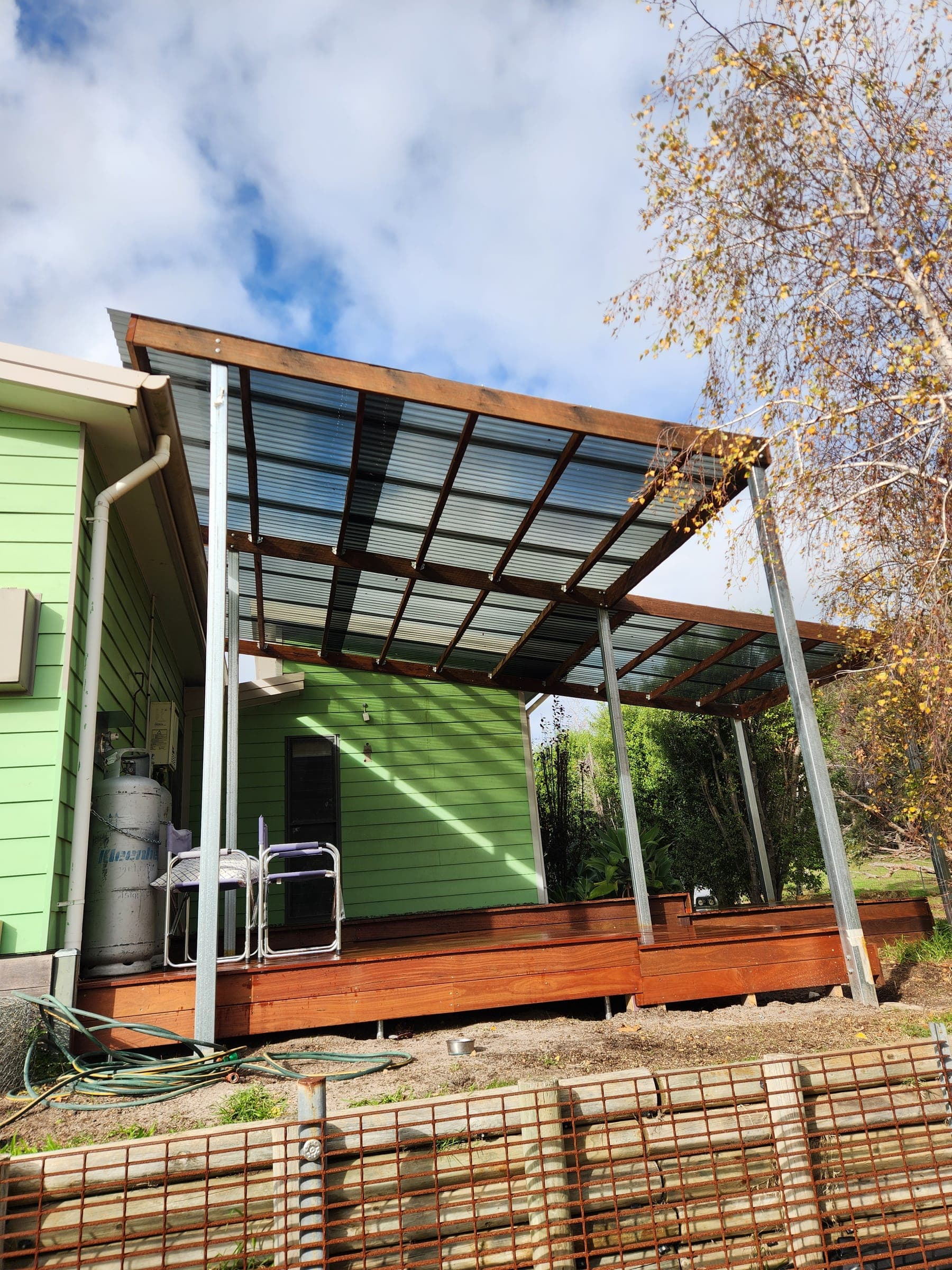 New hardwood deck with a clear patio roof on a green weatherboard house